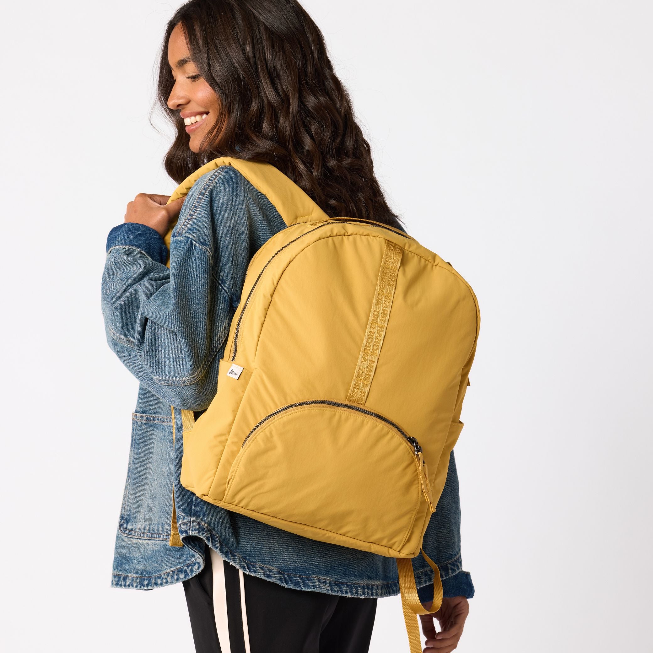Woman wearing mustard travel carry-on backpack full length. #amber_yellow