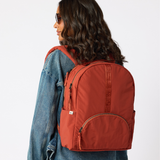  Woman carrying rust travel daypack over shoulder back view. #rust_red