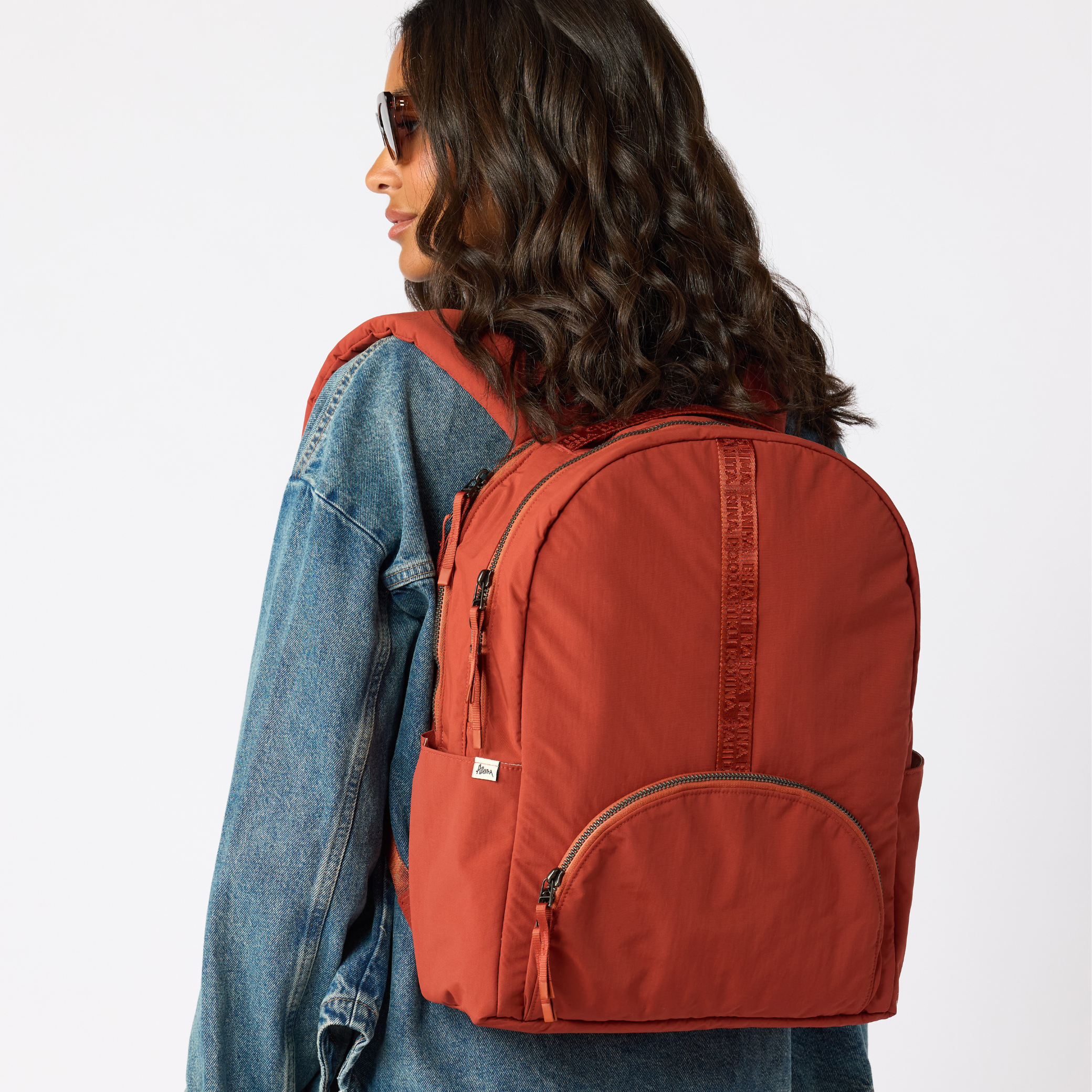  Woman carrying rust travel daypack over shoulder back view. #rust_red
