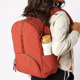 Woman with rust travel backpack water bottle in side pocket. #rust_red
