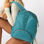 Woman carrying teal travel daypack over one shoulder back view. #solid_teal