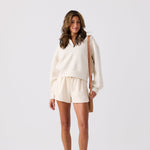 Woman wearing a white outfit with shorts and a beige bag on a light gray background Small nylon shoulder bag with zip compartments for organized storage #camel