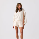 Woman wearing a white outfit with shorts and a beige bag on a light gray background Small nylon shoulder bag with zip compartments for organized storage #camel