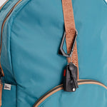 Close-up of a turquoise blue nylon backpack with a tan monogrammed shoulder strap attached to a black car key fob holder. #teal_and_camel