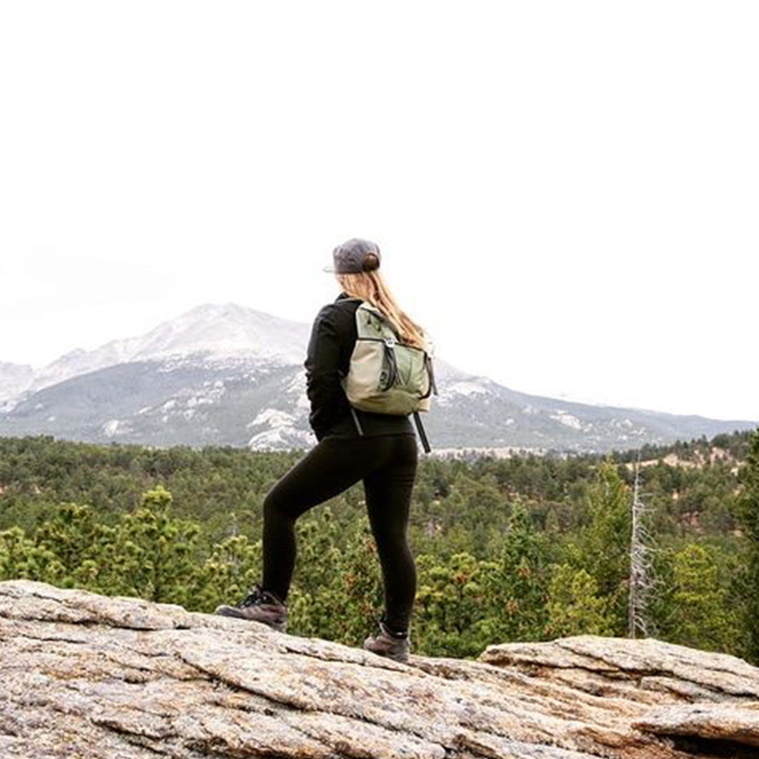 Person hiking on a mountain with a backpack, surrounded by trees and mountains. #olive