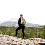 Person hiking on a mountain with a backpack, surrounded by trees and mountains. #olive
