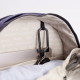 Close-up of the inside of a bag showing a black carabiner clipped to a zipper, with a light beige patterned lining and part of a cream fabric exterior visible. #indigo