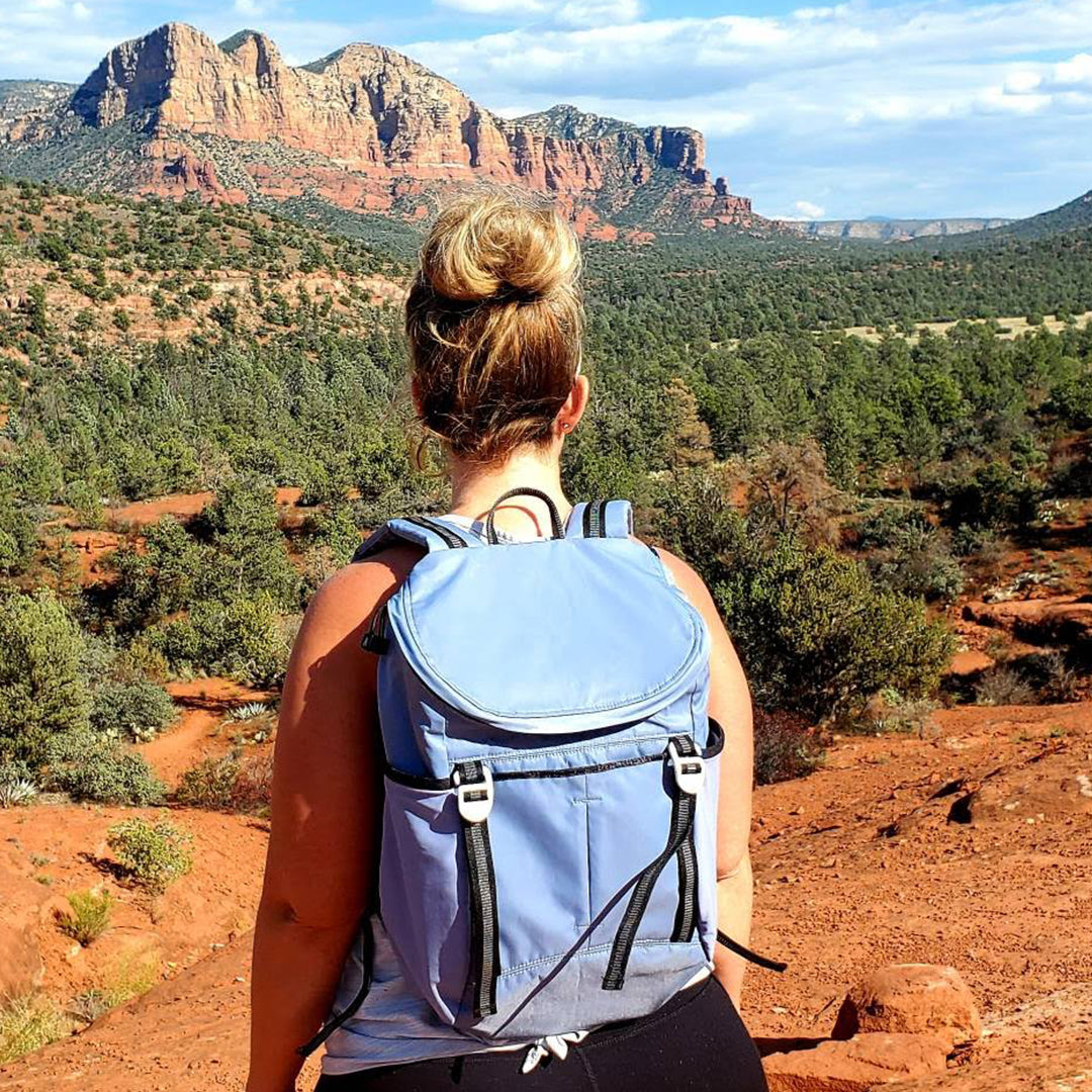 Person with a blue sonu backpack overlooking a scenic landscape with mountains and trees. #slate_blue