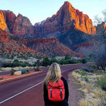 Person with a red backpack standing on a road with a scenic mountain landscape #poppy_red