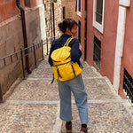 Person with a yellow backpack walking down a narrow street between - buildings. travel backpack #sunflower_yellow